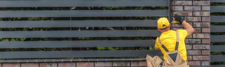 A man in a yellow shirt and hat paints a fence, showcasing his work as a fencing contractor, representing the need for a PPC campaign to get more work.