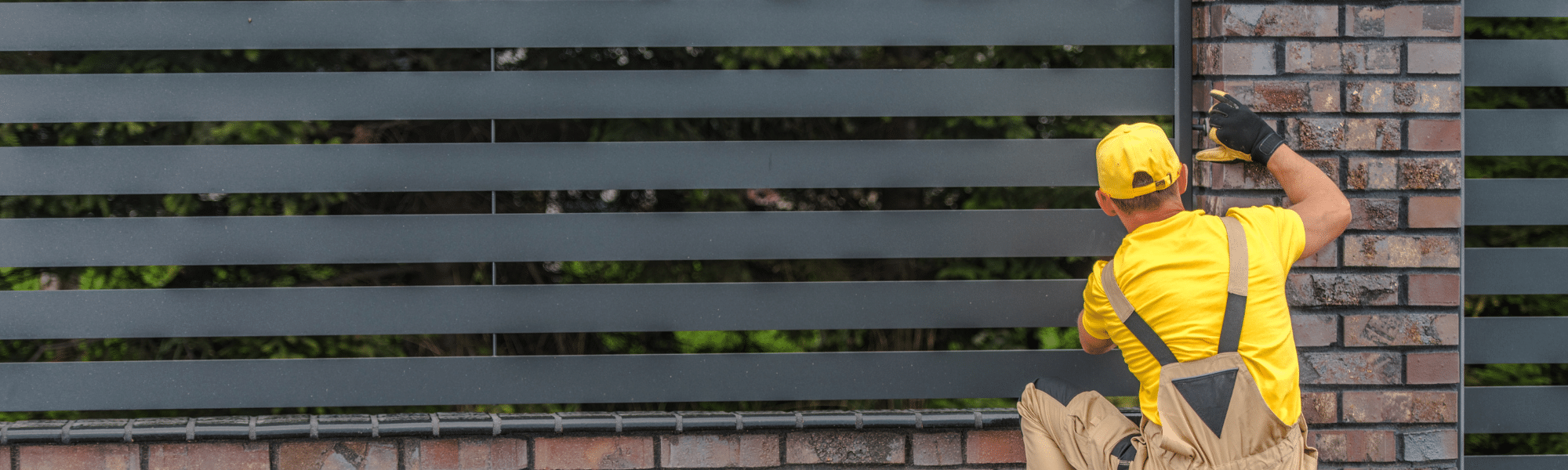 A man in a yellow shirt and hat paints a fence, showcasing his work as a fencing contractor, representing the need for a PPC campaign to get more work.