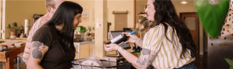 Two women standing in front of a table with a bottle of wine on it, showing a friendly social scene representing local SEO foot traffic.